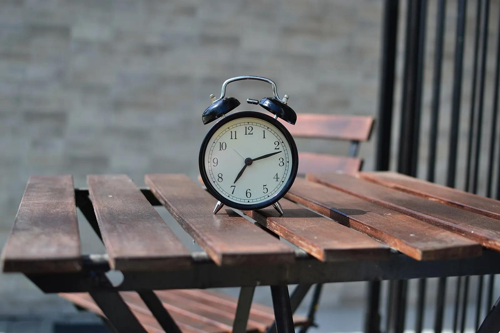 A black alarm clock standing on a wooden slatted table
