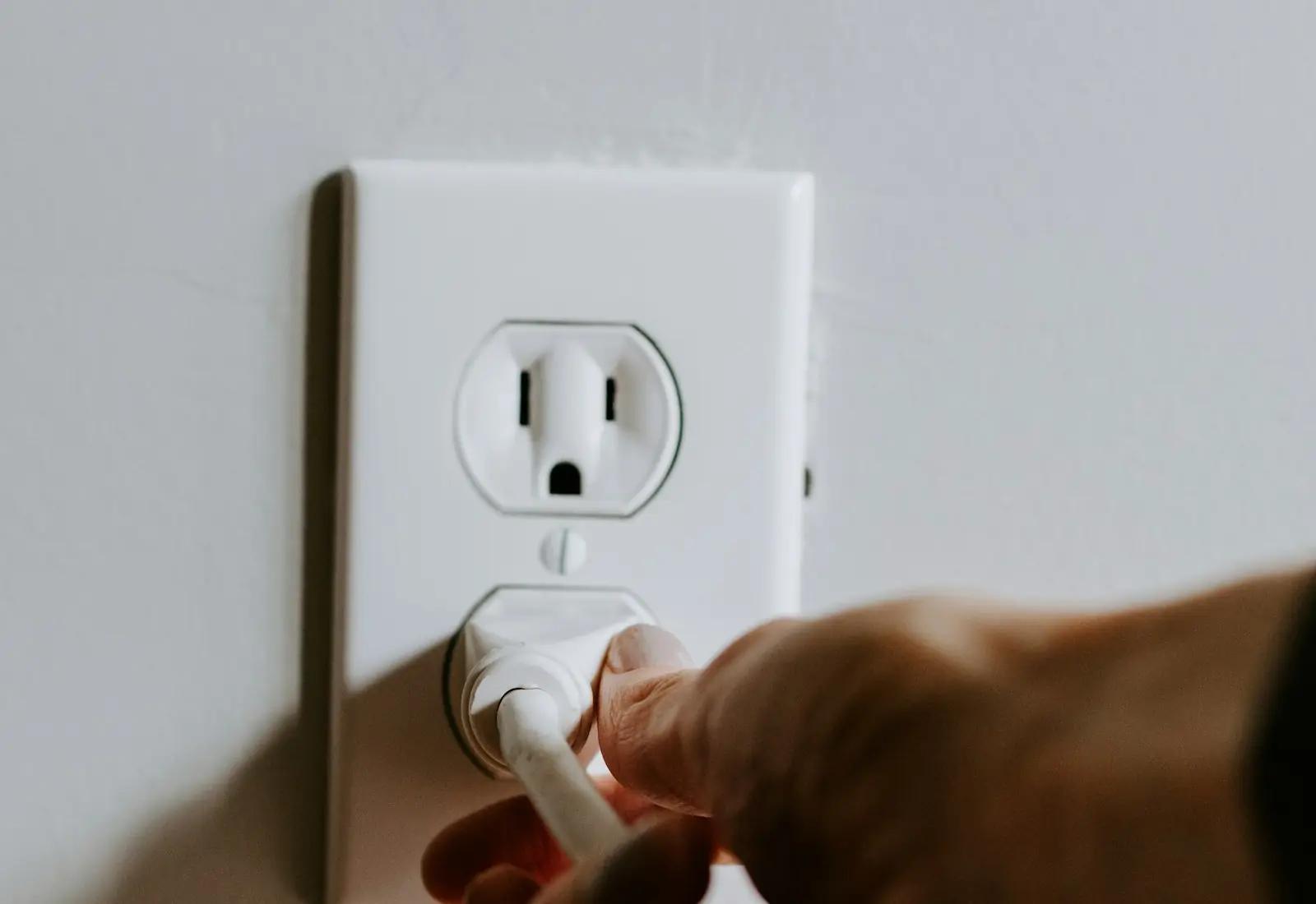 A hand pushing a white plug into a wall outlet