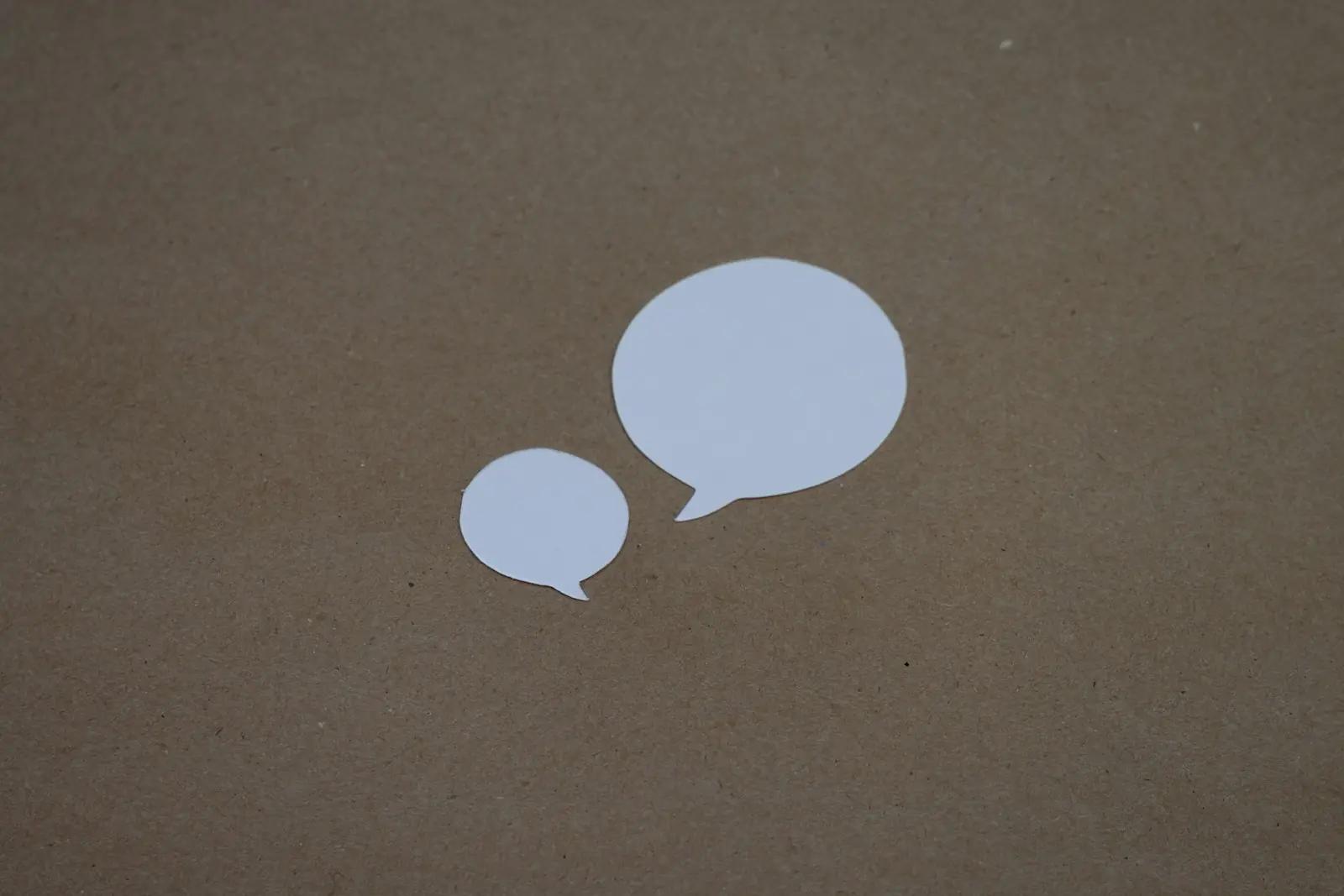 Two paper speech bubbles on a brown background