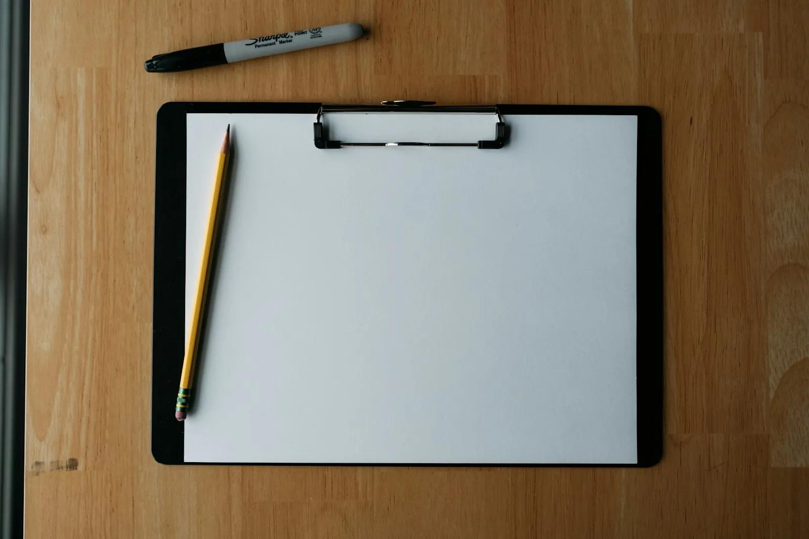 Clipboard, pencil and pen on a wooden surface