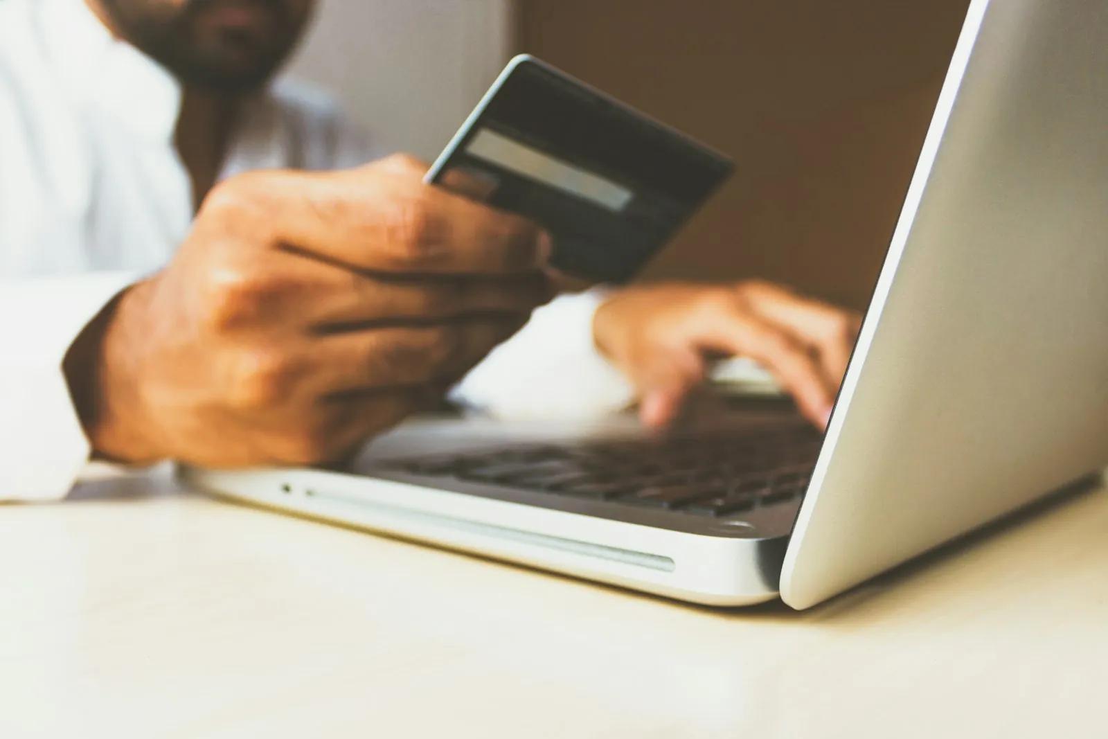 A hand holding a payment card next to a laptop