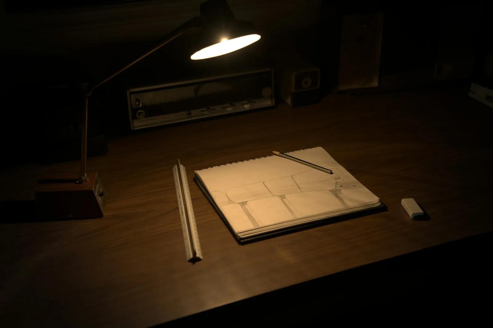 A desk lamp lighting a sketchbook and pencils at night