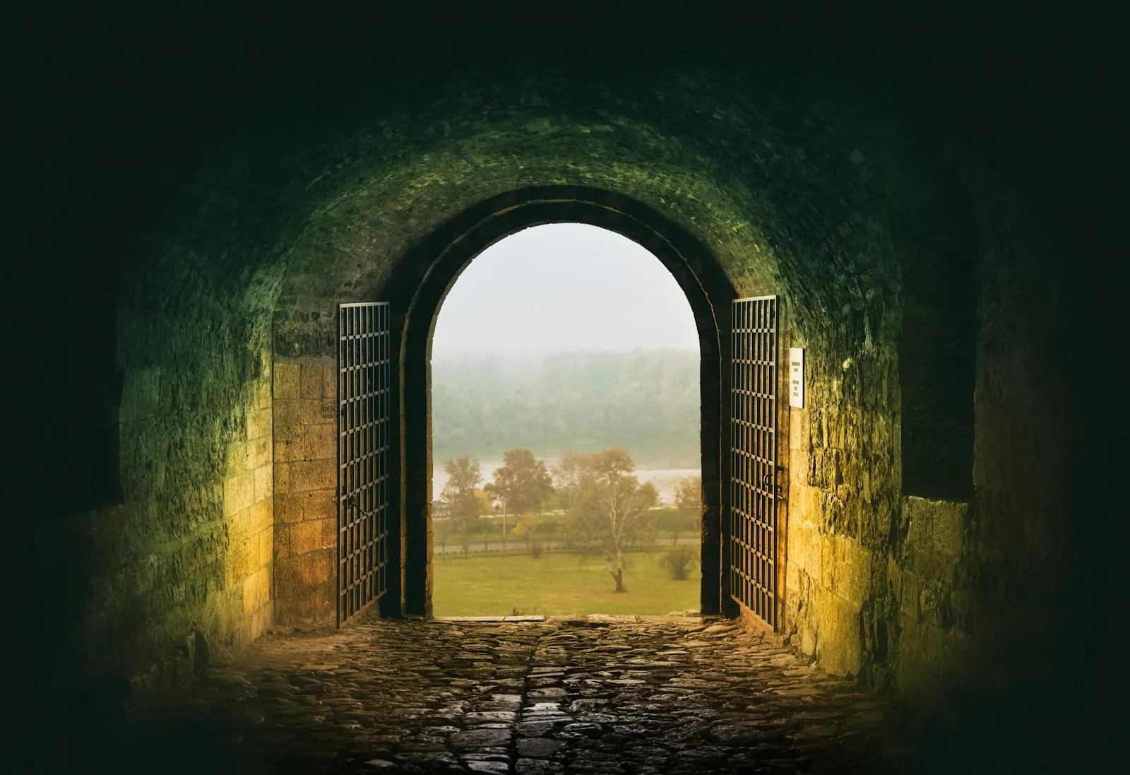 An open arched doorway leading from a dark tunnel into daylight