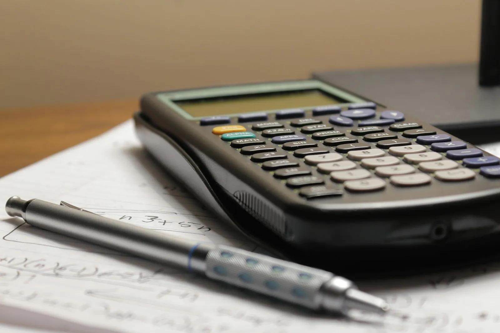 A calculator and a pen on top of handwritten paperwork