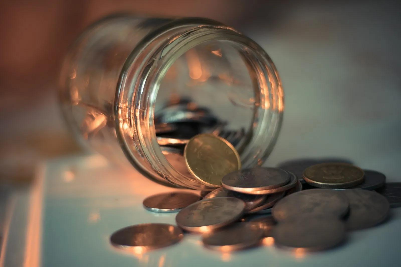 Coins spilling from a tipped-over glass jar