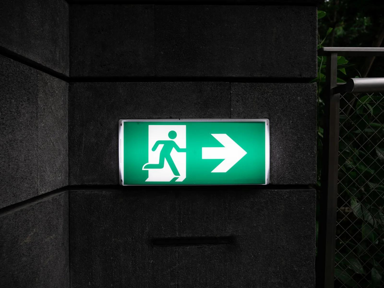 A green illuminated exit sign on a dark wall