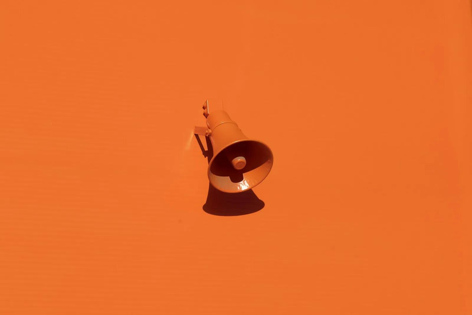 An orange megaphone mounted on an orange wall